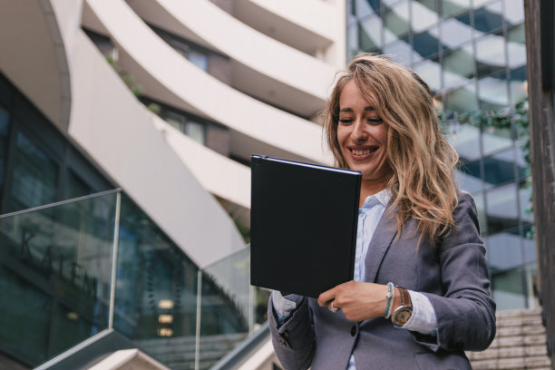 一位女商人站在商业大楼附近，笔记本电脑提高了她的工作效率图片下载