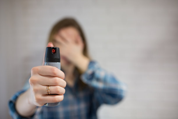 已婚妇女手持胡椒喷雾罐保护自己。女孩用手捂住脸。后面是白色背景。自卫的照片。复制空间位置。图片下载