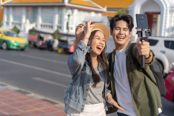 东南亚泰国曼谷街头佛寺前，一男一女旅行者在自拍视频通话的亚洲肖像——无忧无虑的幸福概念图片下载