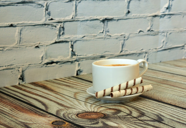 两个华夫饼卷放在碟子上，一杯新鲜的卡布奇诺放在一张轻木桌上。图片下载