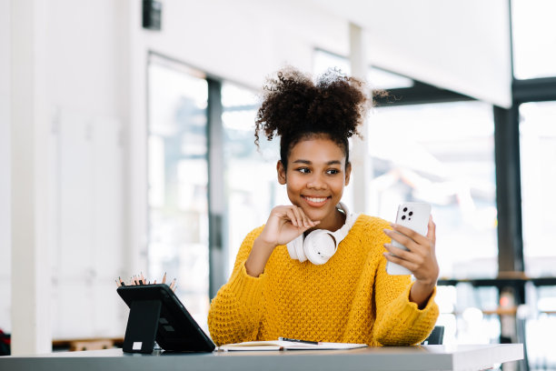 迷人的年轻非洲学生在大学图书馆学习，坐在书桌前，使用笔记本电脑，平板电脑和耳机进行视频聊天。图片下载