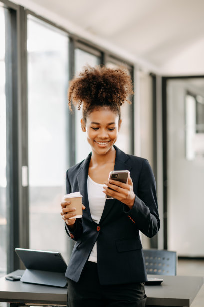 自信美丽的非洲女商人一边在办公室端着咖啡一边用笔记本电脑和数码平板电脑打字图片下载