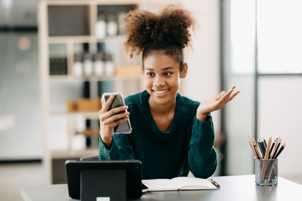 迷人的年轻非洲学生在大学图书馆学习，坐在书桌前，使用笔记本电脑，平板电脑和耳机进行视频聊天。图片下载