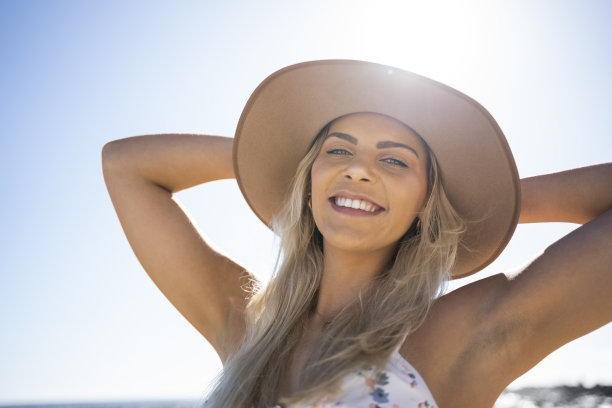 沙滩上穿着比基尼，戴着太阳帽的年轻美女图片下载