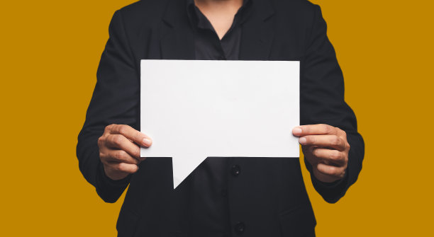 西装革履的商人站在橙色背景上，手里拿着一个空白的白色演讲泡泡图片下载