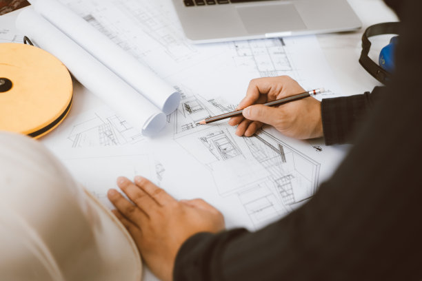 建筑工程师，在办公室用图纸和笔记本电脑工作。施工现场建筑平面图检查。建设项目。顾问施工现场工程师。图片下载