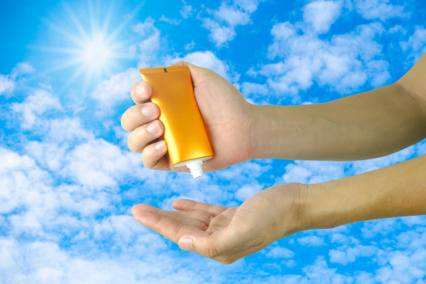一位女士正在涂抹防晒霜和护肤品，以保护皮肤免受紫外线的伤害。她正在给她的手和胳膊涂防晒霜。太阳的标志是一个非常阳光的背景。健康护肤理念图片下载