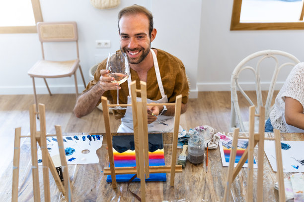 艺术与葡萄酒工作坊。一个中年人在油漆车间喝着白葡萄酒。图片下载