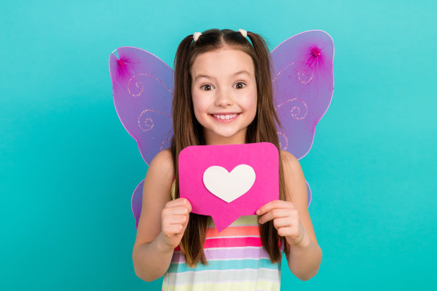 照片兴奋迷人可爱的青春期前的女孩穿着时尚的条纹衣服，手拿粉红色的纸卡孤立在蓝色的背景图片下载