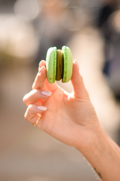 在模糊的背景上，女性手拿着美味的亮绿色马卡龙的特写图片下载