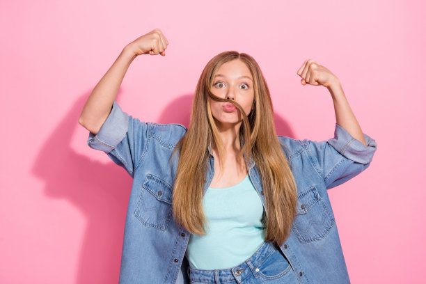有吸引力的年轻女子的照片肖像，拳头，肌肉，胡子，穿着时尚的牛仔衣服，孤立在粉红色的背景图片下载