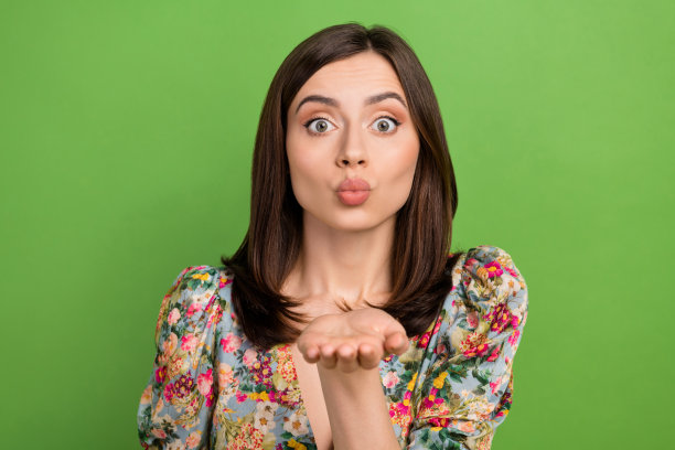 照片迷人的可爱的女士噘起嘴唇，手臂手掌送空气吻你孤立的绿色背景图片下载