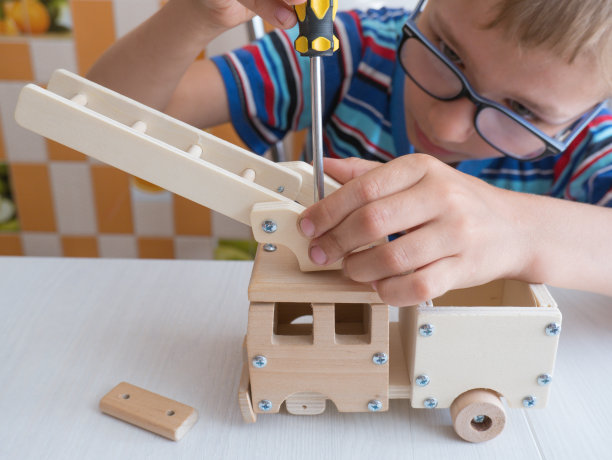 一个7-8岁的男孩坐在厨房的桌子旁，拿着一把螺丝刀，小心翼翼地组装一辆木制汽车。把手收起来图片下载