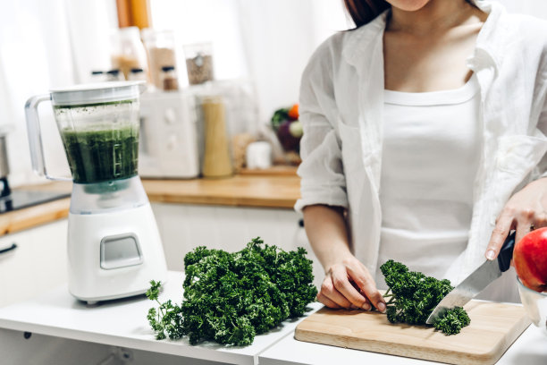 健康的女人喜欢在家里的厨房里用搅拌器制作绿色蔬菜排毒和绿色水果奶昔。节食的概念。健康的生活方式图片下载
