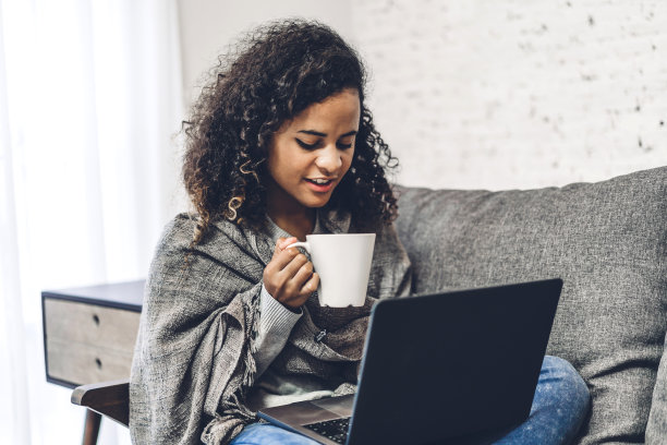 年轻的非裔美国黑人妇女正在放松地使用笔记本电脑。女人一边查看社交软件一边工作。通信与技术概念图片下载