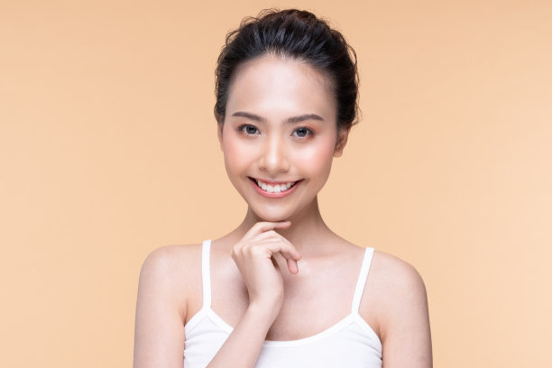 美丽的亚洲年轻女子抚摸柔软的脸颊，微笑，干净新鲜的皮肤，幸福和开朗，积极的情绪，隔离在米色背景，美容化妆品和面部护理概念图片下载