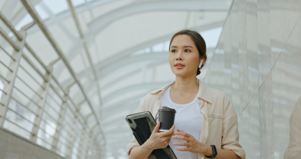 亚洲女商人在上班的路上用蓝牙耳机开会，脸上带着幸福的微笑。妇女使用城市交通路线免费的互联网技术在城市图片下载