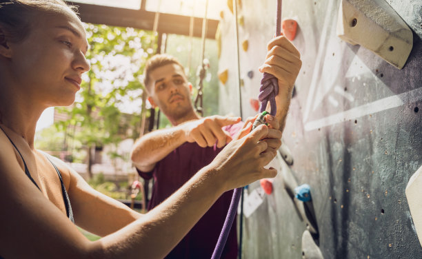 一对强壮的攀登者用彩色的握把和绳索爬上一堵人造墙。图片下载