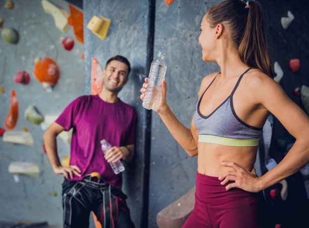 一对强壮的攀登者用彩色的握把和绳索顶着一堵人造墙。图片下载