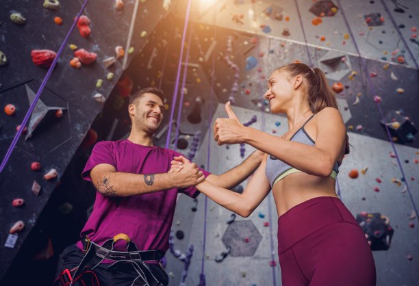 一对强壮的攀登者用彩色的握把和绳索顶着一堵人造墙。图片下载