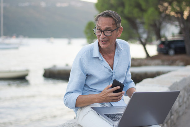 坐在海边用笔记本电脑咨询客户的商人图片下载