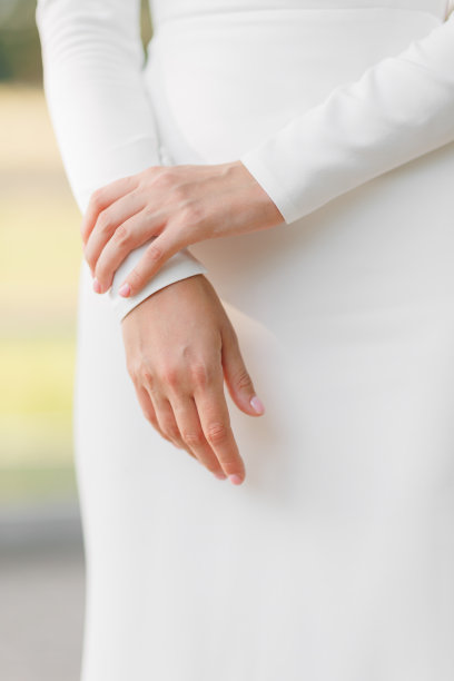 难以辨认的女人在户外穿着优雅的白色婚纱。裁剪照片的女人的手与经典的美甲。时尚时尚的绸缎连衣裙，没有装饰品。婚礼新娘礼服细节。图片下载