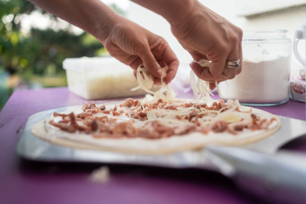 特写:一名妇女在黑色的厨房台面上盖上阿尔萨斯鞑靼蛋糕的面团，旁边是制作火焰鞑靼蛋糕的原料图片下载