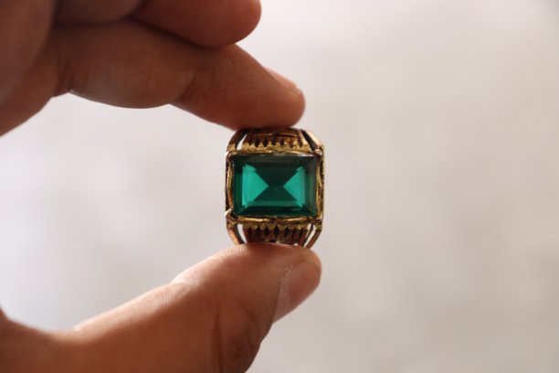 一枚镶嵌着绿色祖母绿宝石的古老金戒指，由人用手指夹住图片下载