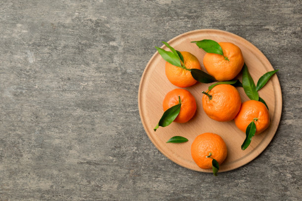 新鲜切好的小柑橘和整个柑橘放在彩色背景的圆形盘子上。准备食品和饮料配料。健康饮食主题俯视图与复制空间图片下载