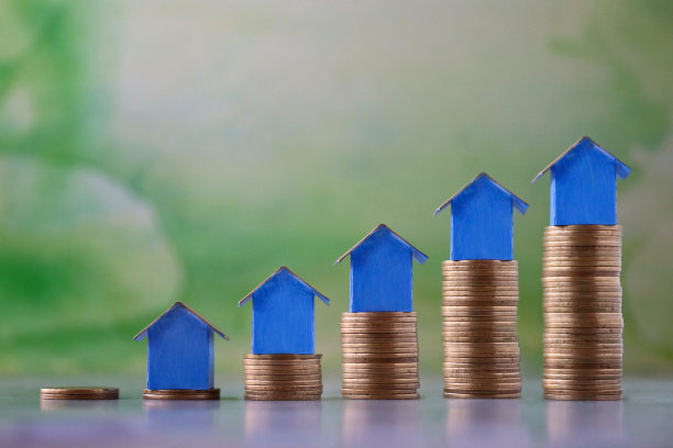 排蓝色纸板房子的特写图像，五颜六色的海滩小屋站在成堆的硬币上，重点放在前景，斑驳的绿色背景，家庭财务，房地产和假日储蓄概念图片下载