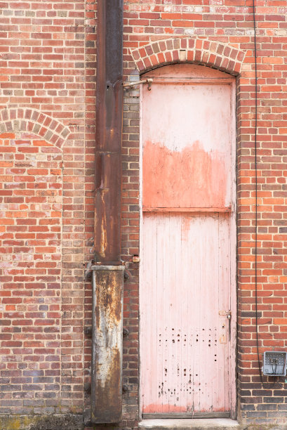 老砖工业建筑里的一扇褪色、破烂的窄木门。图片下载