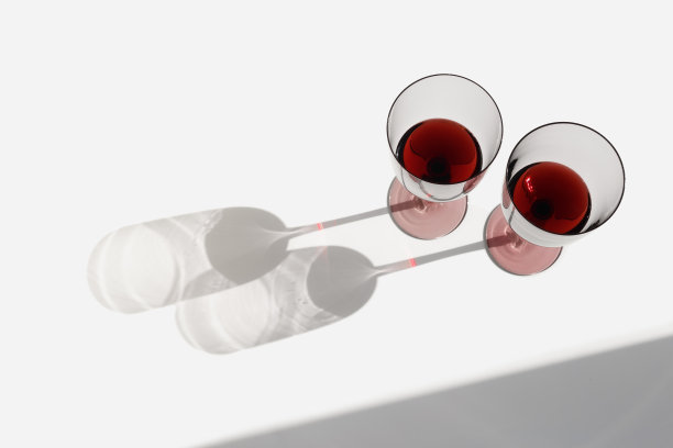 最小的夏日场景与一杯红酒，阳光的阴影在白色的背景，copyspace，酒杯平放。两个酒杯，酒精饮料的照片。假期，聚会，活动的概念图片下载