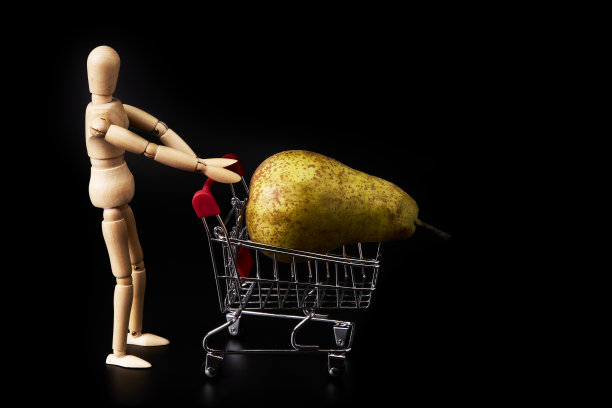 假人推着购物车，黑色背景上有一个梨子。健康的购物图片下载