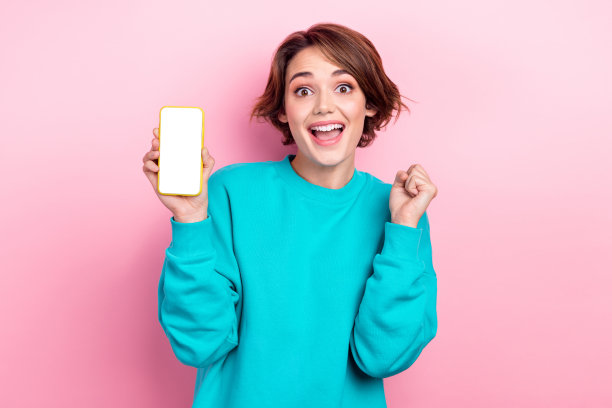 开朗可爱的女孩的肖像，穿着时尚的青色衣服，手持小工具，快乐的购物销售孤立在粉红色的背景图片下载