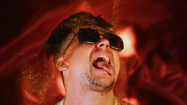 勇敢的人把闪光的微粒洒在自己身上。魅力奢华的照片，闪亮的脸，张开的嘴。富观肖像男人们戴着墨镜，脸上洒满了金色的光芒。图片下载