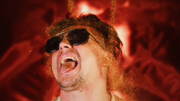 勇敢的人把闪光的微粒洒在自己身上。魅力奢华的照片，闪亮的脸，张开的嘴。富观肖像男人们戴着墨镜，脸上洒满了金色的光芒。图片下载