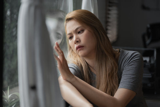 一个沮丧的女人坐在一个大窗户旁边，用手触摸着窗户玻璃，沉思着，脸上带着悲伤的表情图片下载