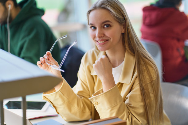 快乐的女学生拿着眼镜坐在大学的课桌前。肖像图片下载