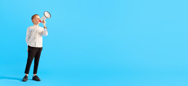 小男孩，穿着白衬衫和黑裤子的孩子，在蓝色的摄影棚背景下用扩音器说话。新闻、信息图片下载