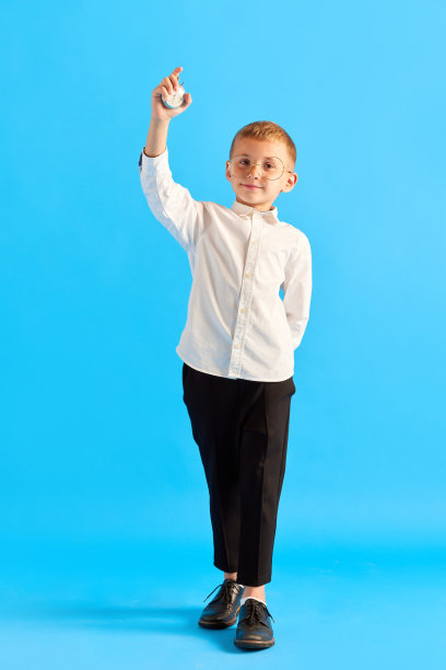 回到上学时间。小男孩，戴眼镜的孩子，白衬衫和黑裤子，在蓝色的工作室背景下拿着时钟图片下载