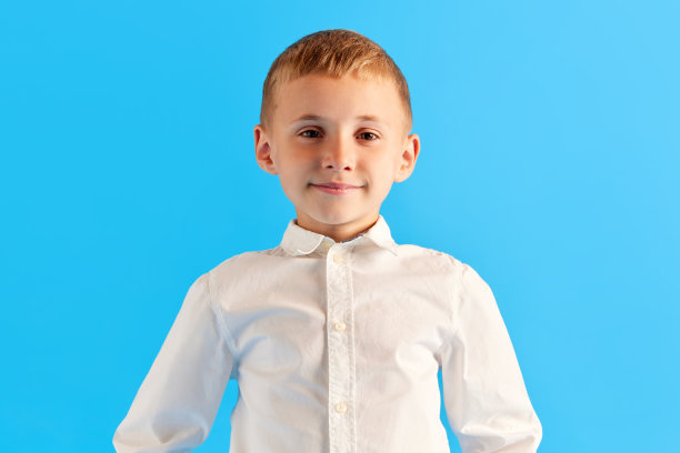 小男孩的肖像，小学生，孩子穿着白衬衫，在蓝色的工作室背景下微笑着看着相机图片下载
