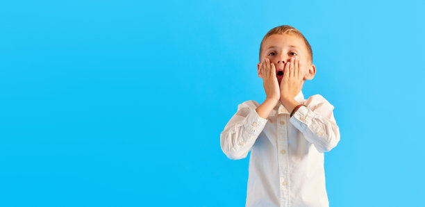 情绪化的小男孩，孩子，小学生，穿着白衬衫，满脸震惊地站在蓝色的画室背景下图片下载