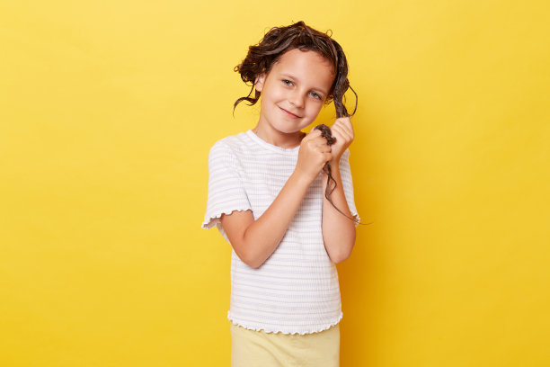 可爱可爱的小女孩，湿头发上涂着洗发水，穿着白色t恤，孤立地站在黄色背景下洗头发，看着镜头卫生程序。图片下载
