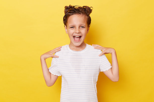 惊讶的小女孩，湿头发上涂着洗发水，穿着白色t恤，独自站在黄色的背景下，一边做洗澡程序，一边开心地大喊大叫，表达幸福。图片下载