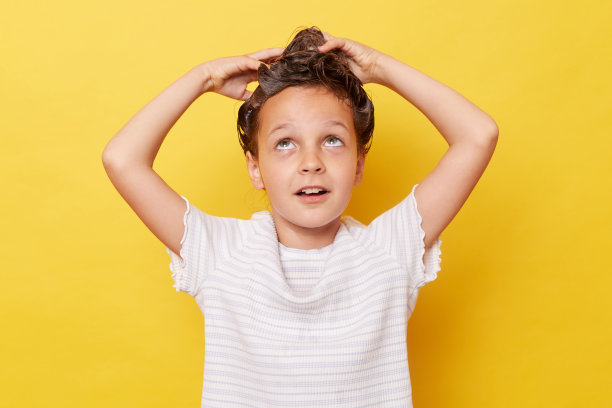 有趣的小女孩用洗发水洗头，抬头看，穿着白色t恤，在黄色的背景下进行洗澡卫生程序图片下载