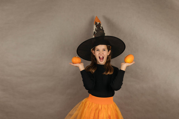 一个有趣的十几岁女孩的特写肖像，在灰色背景上穿着女巫服装，手里拿着南瓜图片下载