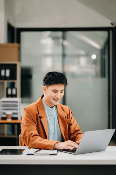 年轻的亚洲商人在办公室用笔记本电脑、平板电脑和在纸上做笔记。图片下载