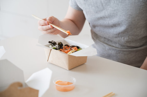 不知名的男子吃着与鲑鱼、鳄梨、海藻等一起的poke bowl。亚洲外卖图片下载