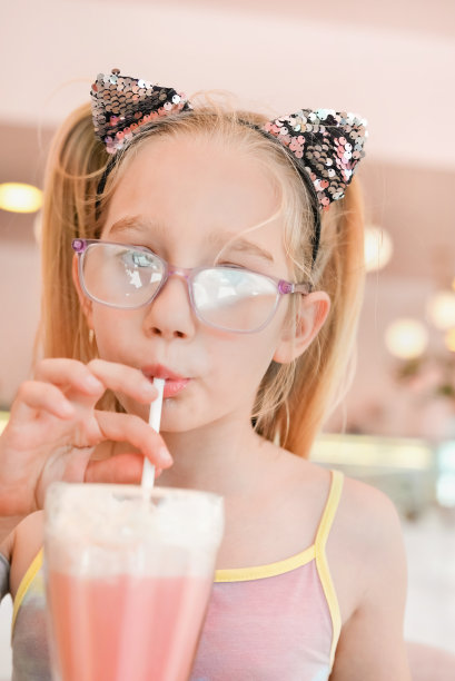 七岁的小女孩在咖啡店用吸管喝草莓奶昔。快乐的女孩用吸管喝鸡尾酒的画像图片下载