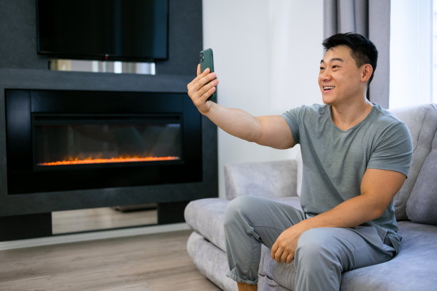 一个快乐的亚洲年轻人坐在家里的沙发上，通过视频通话交流，或者用手机自拍图片下载